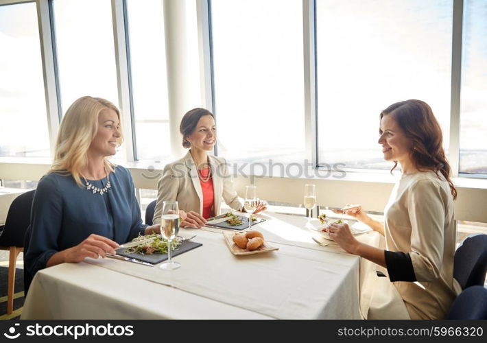 people, holidays, celebration and lifestyle concept - happy women eating and drinking champagne at restaurant