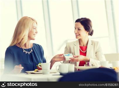 people, holidays, celebration and lifestyle concept - happy women giving birthday present at restaurant