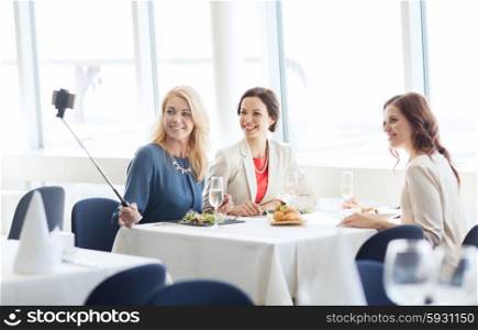 people, holidays, celebration and lifestyle concept - happy women with smartphone selfie stick taking picture at restaurant