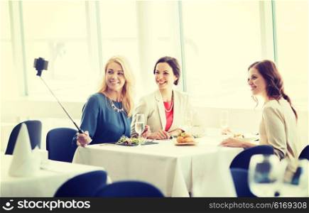 people, holidays, celebration and lifestyle concept - happy women with smartphone selfie stick taking picture at restaurant