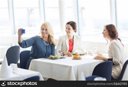 people, holidays, celebration and lifestyle concept - happy women with smartphone taking selfie at restaurant