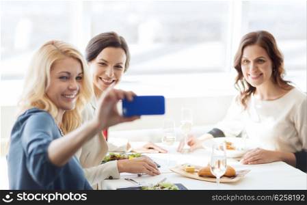 people, holidays, celebration and lifestyle concept - happy women with smartphone taking selfie at restaurant