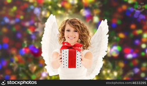 people, holidays, christmas and birthday concept - happy young woman with angel wings holding gift box over lights background