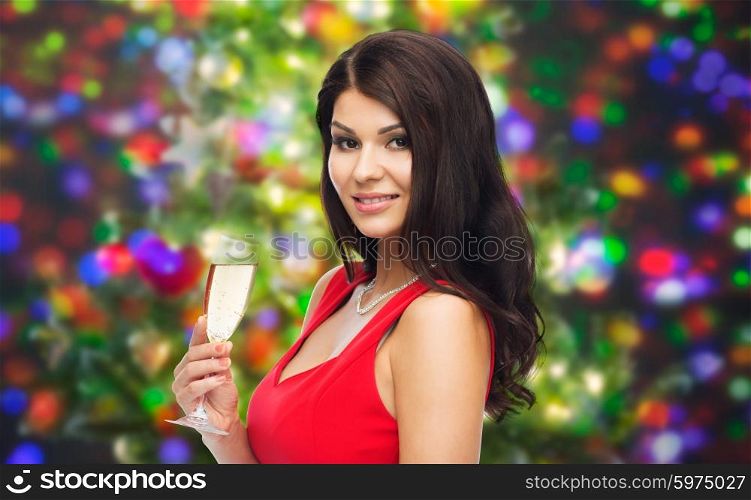 people, holidays, christmas and celebration concept - beautiful sexy woman in red dress with champagne glass over party lights background