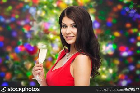 people, holidays, christmas and celebration concept - beautiful sexy woman in red dress with champagne glass over party lights background