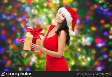 people, holidays, christmas and celebration concept - beautiful sexy woman in red dress and santa hat with gift box over party lights background