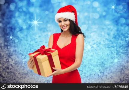 people, holidays, christmas and celebration concept - beautiful sexy woman in red dress and santa hat with gift box over blue glitter and lights background