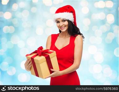 people, holidays, christmas and celebration concept - beautiful sexy woman in red dress and santa hat with gift box over blue lights background