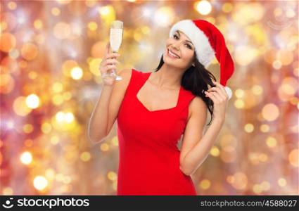 people, holidays, christmas and celebration concept - beautiful sexy woman in santa hat and red dress with champagne glass over lights background
