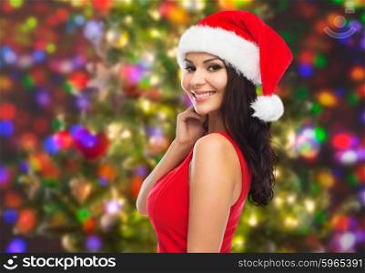 people, holidays, christmas and celebration concept - beautiful sexy woman in santa hat and red dress over holidays lights background