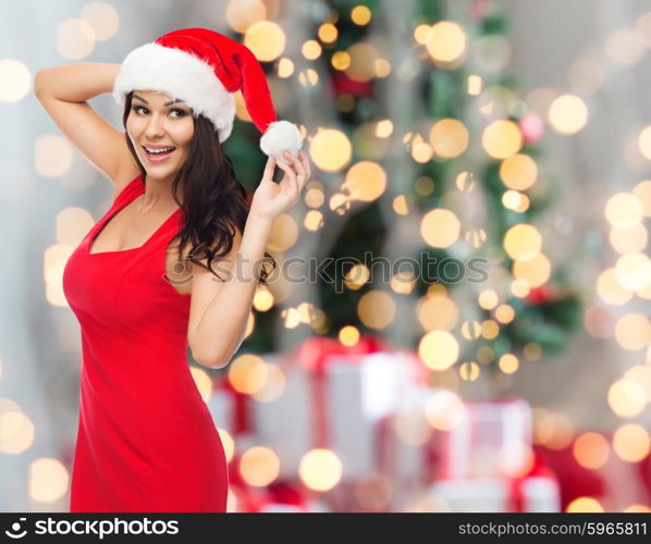 people, holidays, christmas and celebration concept - beautiful sexy woman in santa hat and red dress over lights background