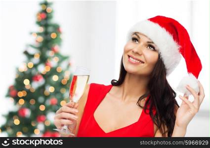 people, holidays, christmas and celebration concept - beautiful sexy woman in santa hat and red dress with champagne glass over room with christmas tree background