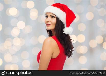 people, holidays, christmas and celebration concept - beautiful sexy woman in santa hat and red dress over lights background