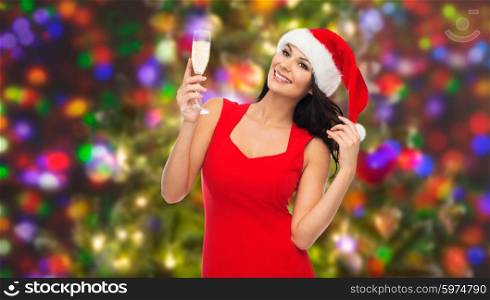 people, holidays, christmas and celebration concept - beautiful sexy woman in santa hat and red dress with champagne glass over lights background