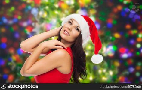 people, holidays, christmas and celebration concept - beautiful sexy woman in santa hat and red dress over party lights background
