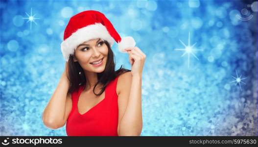 people, holidays, christmas and celebration concept - beautiful sexy woman in santa hat and red dress over blue glitter and lights background