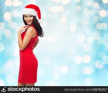 people, holidays, christmas and celebration concept - beautiful sexy woman in santa hat and red dress over blue lights background