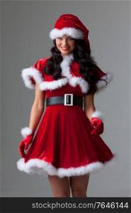 People, holidays, christmas and celebration concept - beautiful sexy woman in santa hat and red dress on gray background. Woman in santa hat and dress