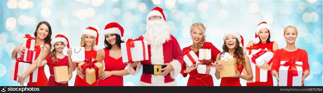 people, holidays, christmas and celebration concept - santa calaus and happy women with gift boxes over blue holidays lights background