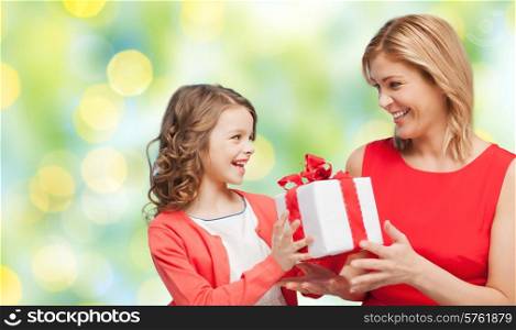 people, holidays, christmas and family concept - happy mother and daughter giving and receiving gift box over green lights background