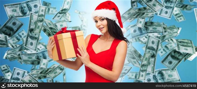 people, holidays, christmas and finances concept - beautiful sexy woman in red dress and santa hat with gift box over dollar money rain on blue background