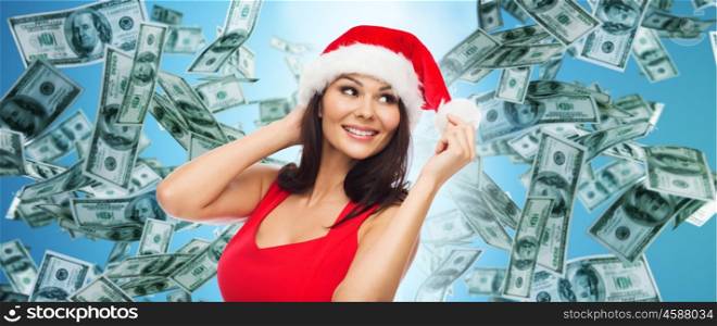 people, holidays, christmas and finances concept - beautiful sexy woman in santa hat and red dress over dollar money rain on blue background