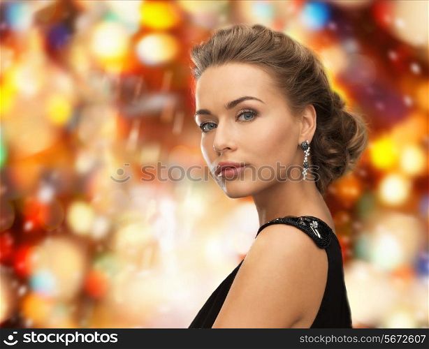 people, holidays, christmas and glamour concept - beautiful woman in evening dress wearing earrings over red lights background