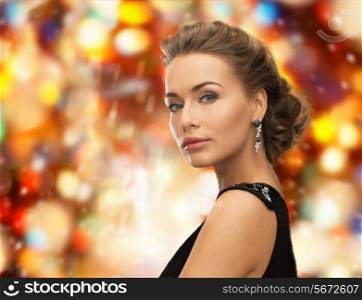 people, holidays, christmas and glamour concept - beautiful woman in evening dress wearing earrings over red lights background