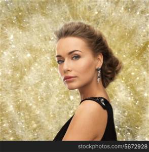 people, holidays, christmas and glamour concept - beautiful woman in evening dress wearing earrings over yellow lights background