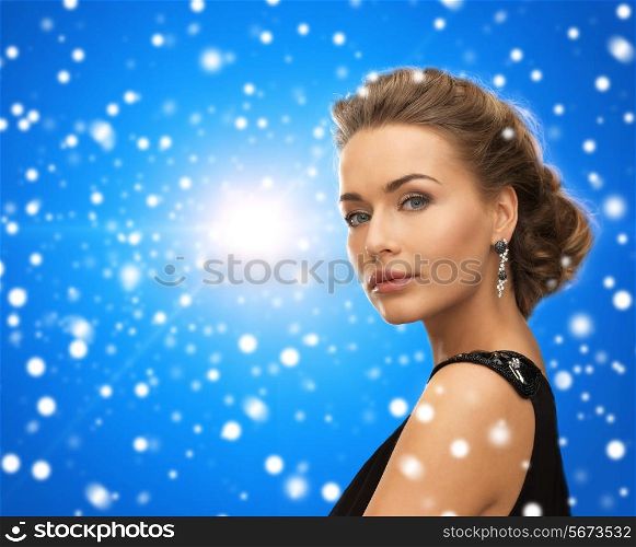 people, holidays, christmas and glamour concept - beautiful woman in evening dress wearing earrings over blue snowy background
