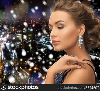 people, holidays, christmas and glamour concept - beautiful woman in evening dress wearing ring and earrings over snowy night city background