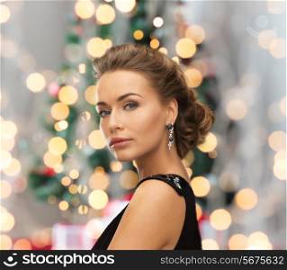 people, holidays, christmas and glamour concept - beautiful woman in evening dress wearing earrings over christmas tree and lights background