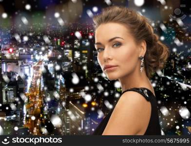 people, holidays, christmas and glamour concept - beautiful woman in evening dress wearing earrings over snowy night background