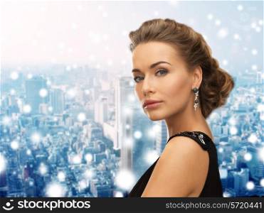 people, holidays, christmas and glamour concept - beautiful woman in evening dress wearing earrings over snowy background