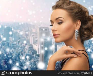 people, holidays, christmas and glamour concept - beautiful woman in evening dress wearing ring and earrings over snowy city background