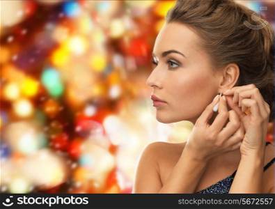 people, holidays, christmas and glamour concept - close up of beautiful woman wearing earrings over red lights background