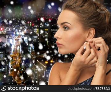 people, holidays, christmas and glamour concept - close up of beautiful woman wearing earrings over snowy night city background