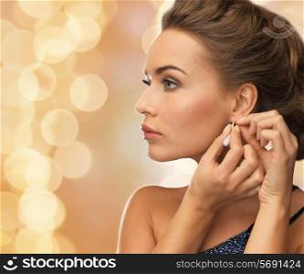 people, holidays, christmas and glamour concept - close up of beautiful woman wearing earrings over beige lights background