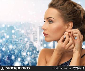 people, holidays, christmas and glamour concept - close up of beautiful woman wearing earrings over snowy city background