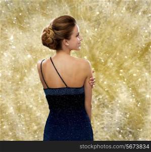 people, holidays, christmas, and glamour concept - smiling woman in evening dress over yellow lights background from back