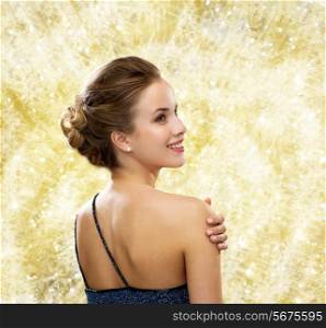 people, holidays, christmas and glamour concept - smiling woman in evening dress showing earrings over yellow lights background