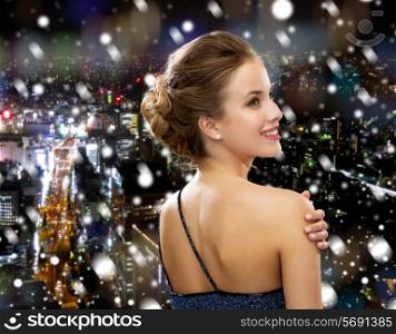 people, holidays, christmas and glamour concept - smiling woman in evening dress showing earrings over snowy night city background