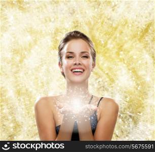 people, holidays, christmas and magic concept - laughing woman in evening dress holding something over yellow lights background