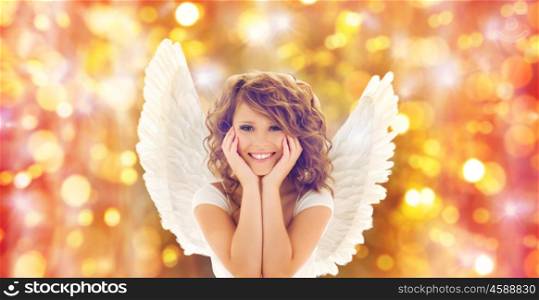 people, holidays, christmas and party concept - happy young woman or teen girl with angel wings over lights background