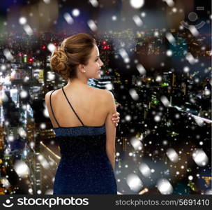 people, holidays, christmas and people concept - smiling woman in evening dress over snowy night city background from back