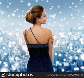 people, holidays, christmas and people concept - smiling woman in evening dress over snowy city background from back