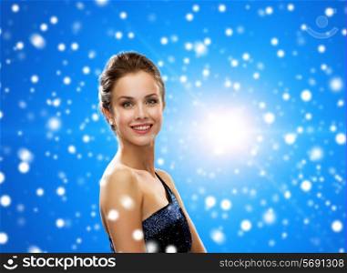 people, holidays, christmas and people concept - smiling woman in evening dress over blue snowy background