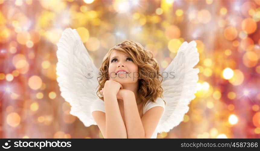 people, holidays, christmas and religious concept - happy young woman or teen girl with angel wings over lights background