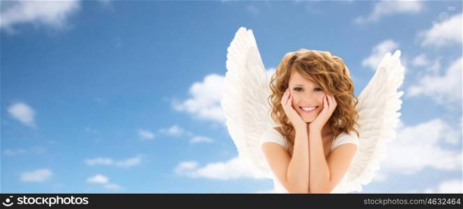 people, holidays, christmas and religious concept - happy young woman or teen girl with angel wings over blue sky and clouds background