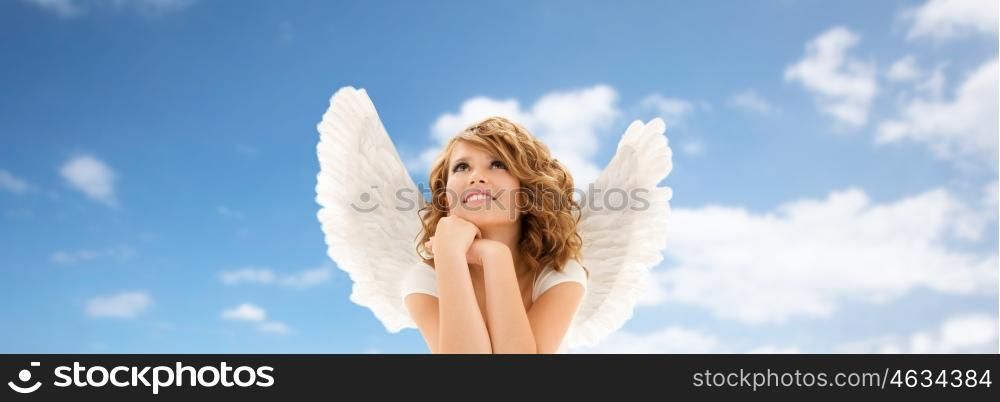 people, holidays, christmas and religious concept - happy young woman or teen girl with angel wings over blue sky and clouds background